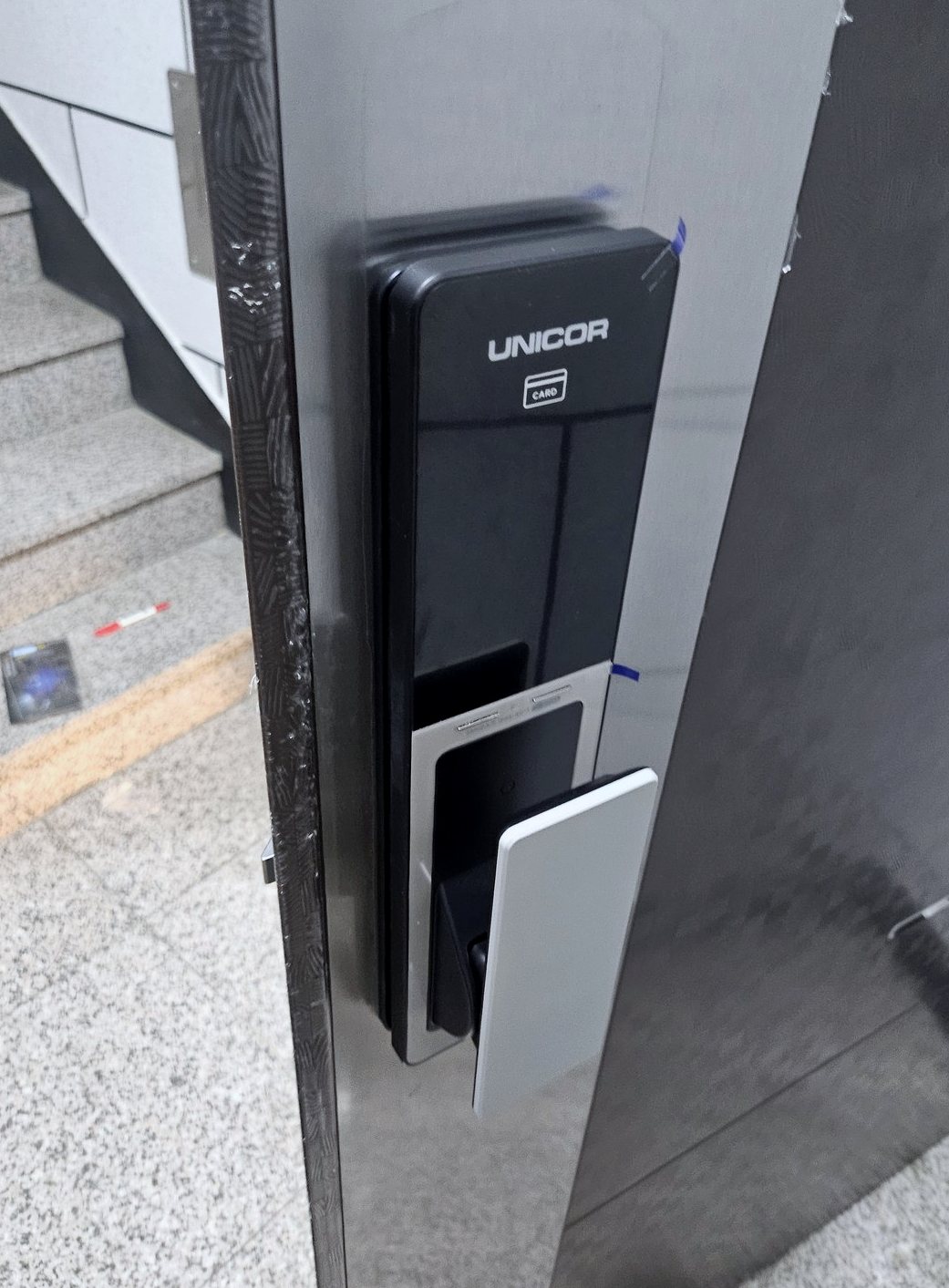 양천구 신월3동 출장 — 은색 금속 문에 단 검은 푸시풀 도어락, 아래쪽 흰 당김 손잡이와 앞면 필름의 파란 띠